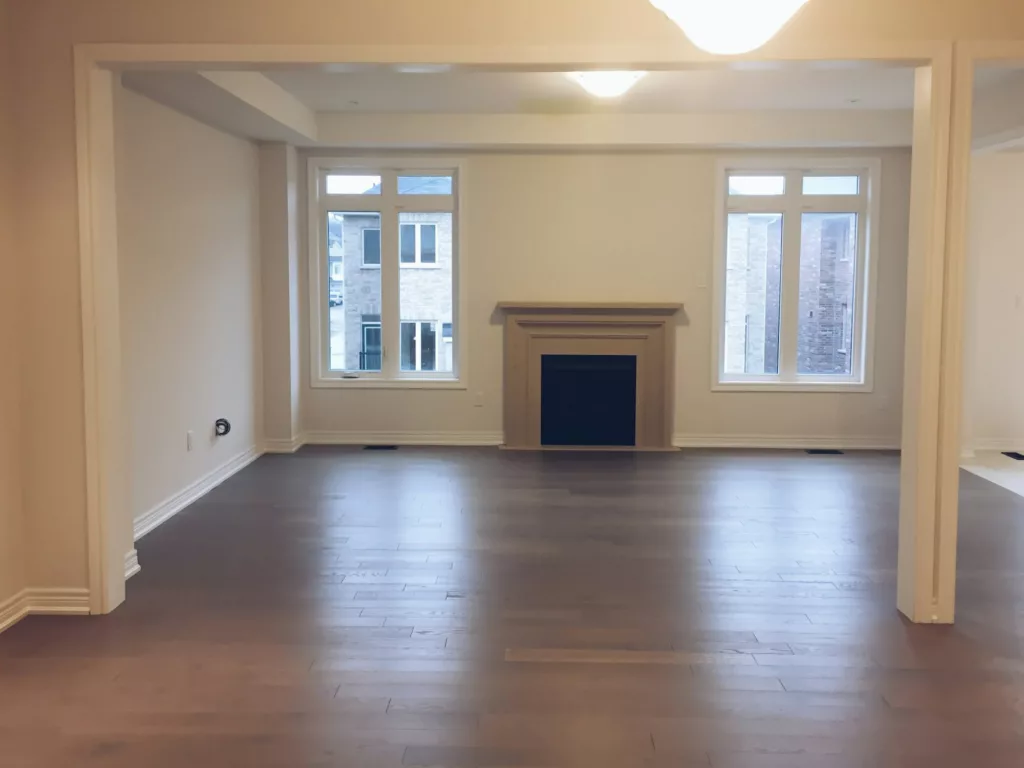 An empty living room with a fireplace and newly installed flooring in a new house